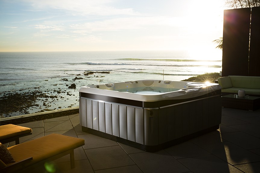 a utopia tahitian hot tub sits on the edge of an oceanside patio as the sun sets over the water